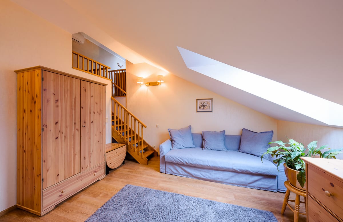 Mansard studio with a pine wardrobe, a sofa bed and the staircase behind