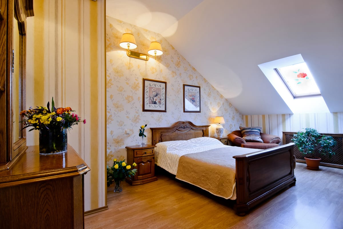 Mansard bedroom under a sloping ceiling, carved sleigh bed, skylight and yellow flowers in a vase