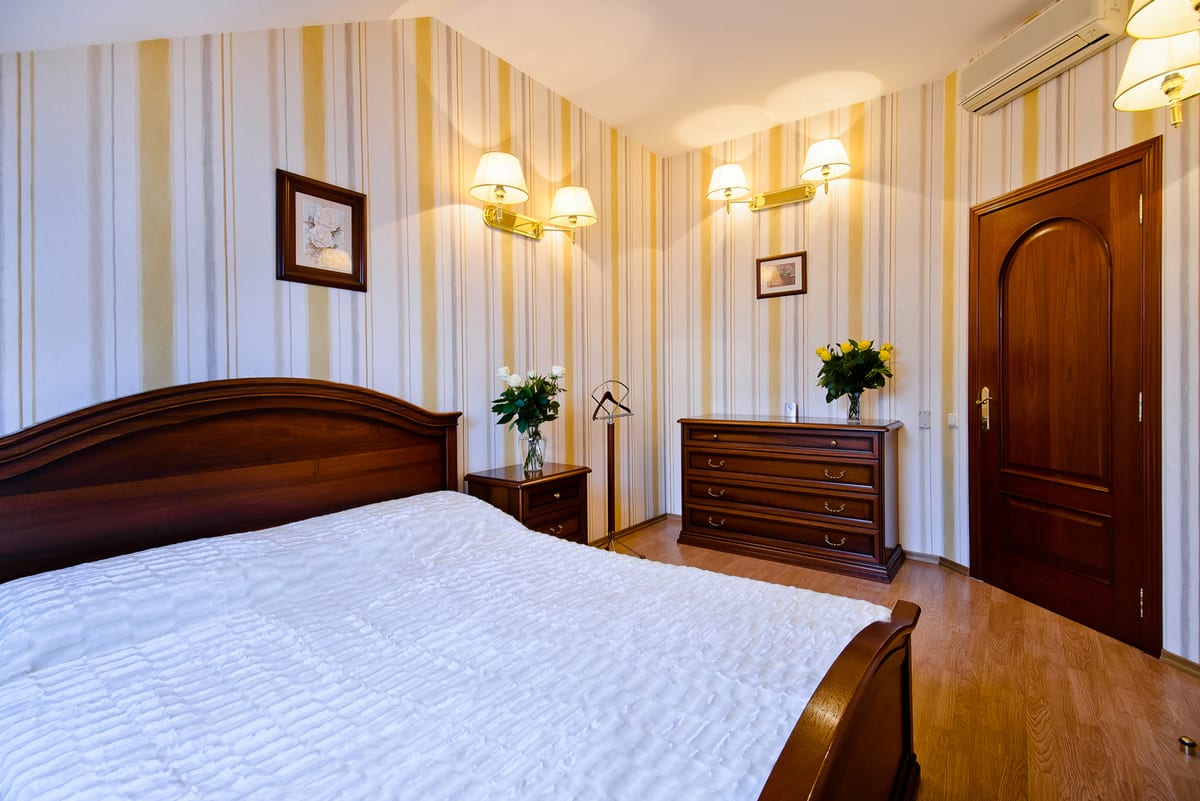 Mansard bedroom with striped wallpaper, a chest of drawers and a white-covered double bed