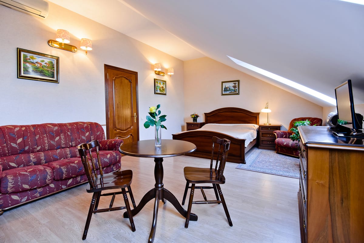 Open mansard studio: a raspberry patterned sofa, a round dining table and a double bed