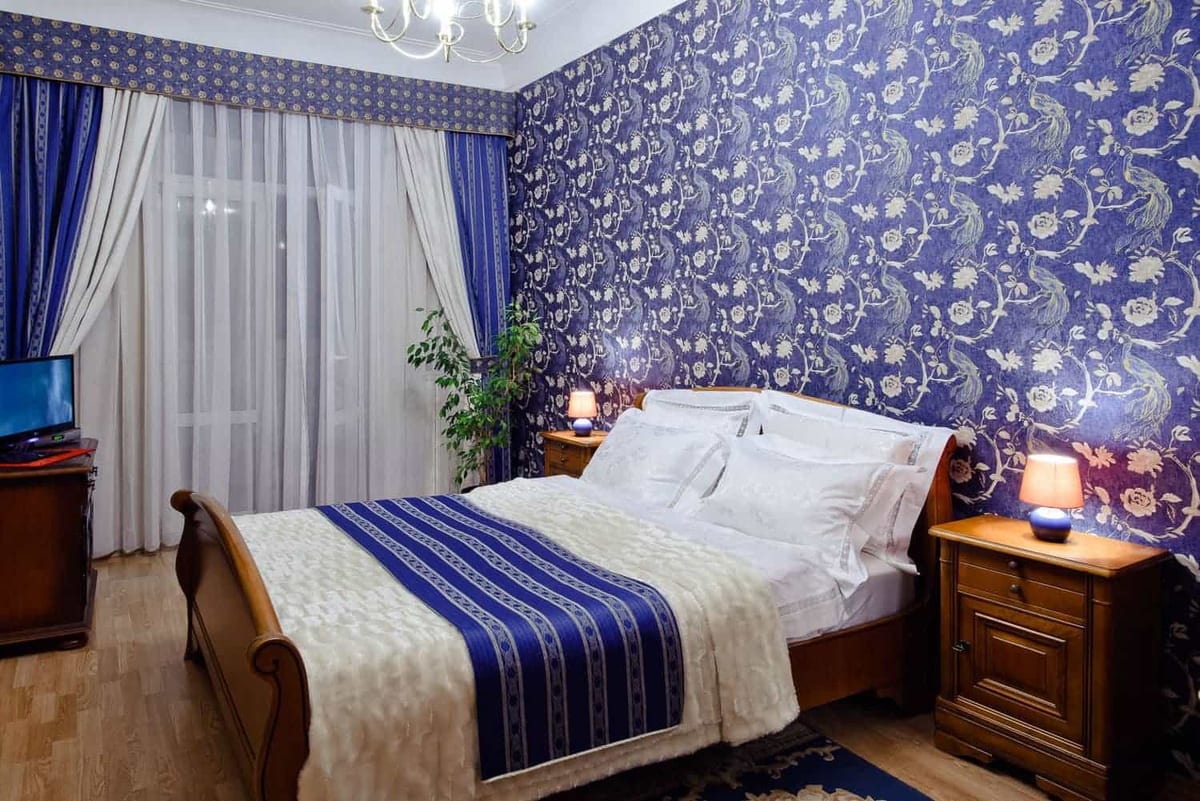 Bedroom with cobalt damask wallpaper, a chandelier and a blue runner across the bed