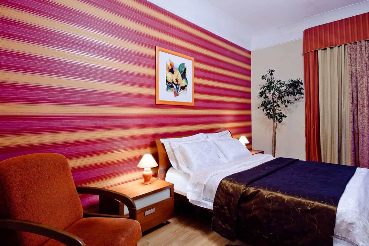 Raspberry-striped bedroom with an orange armchair, a framed print and a double bed