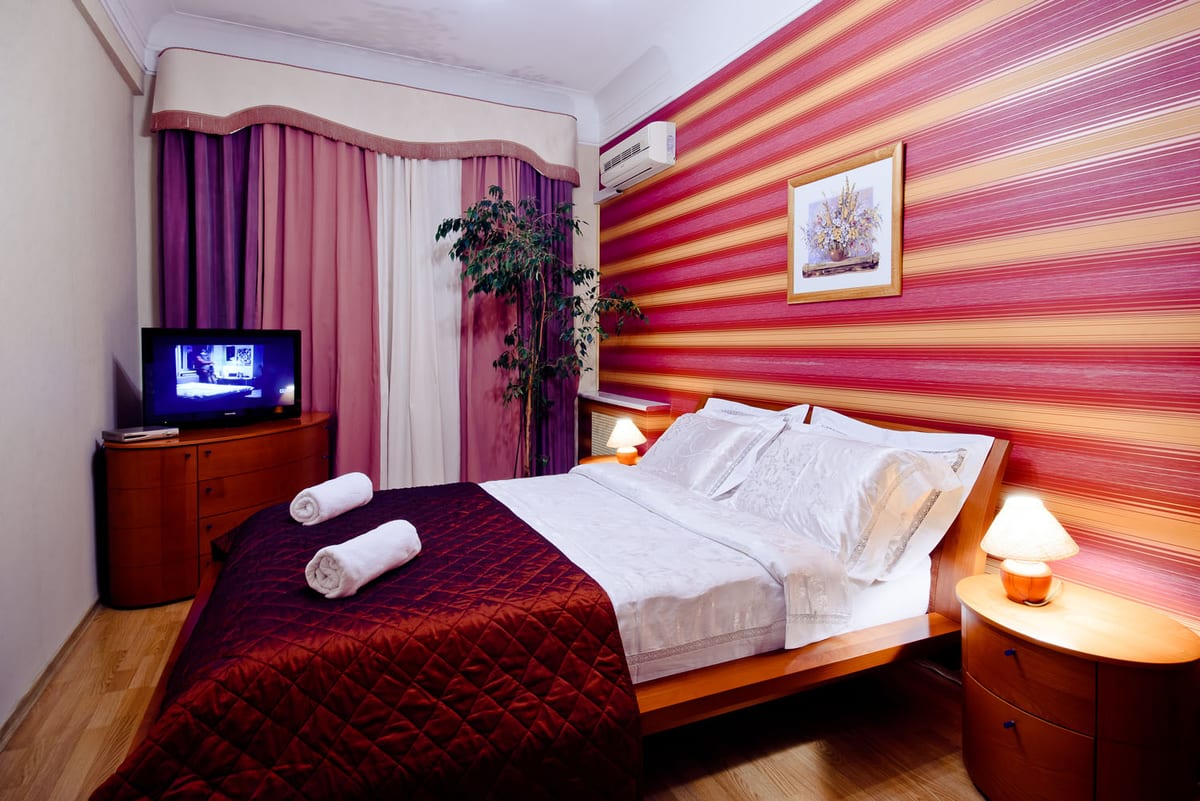 Raspberry-striped bedroom, wall-mounted television and rolled towels on a claret bedspread