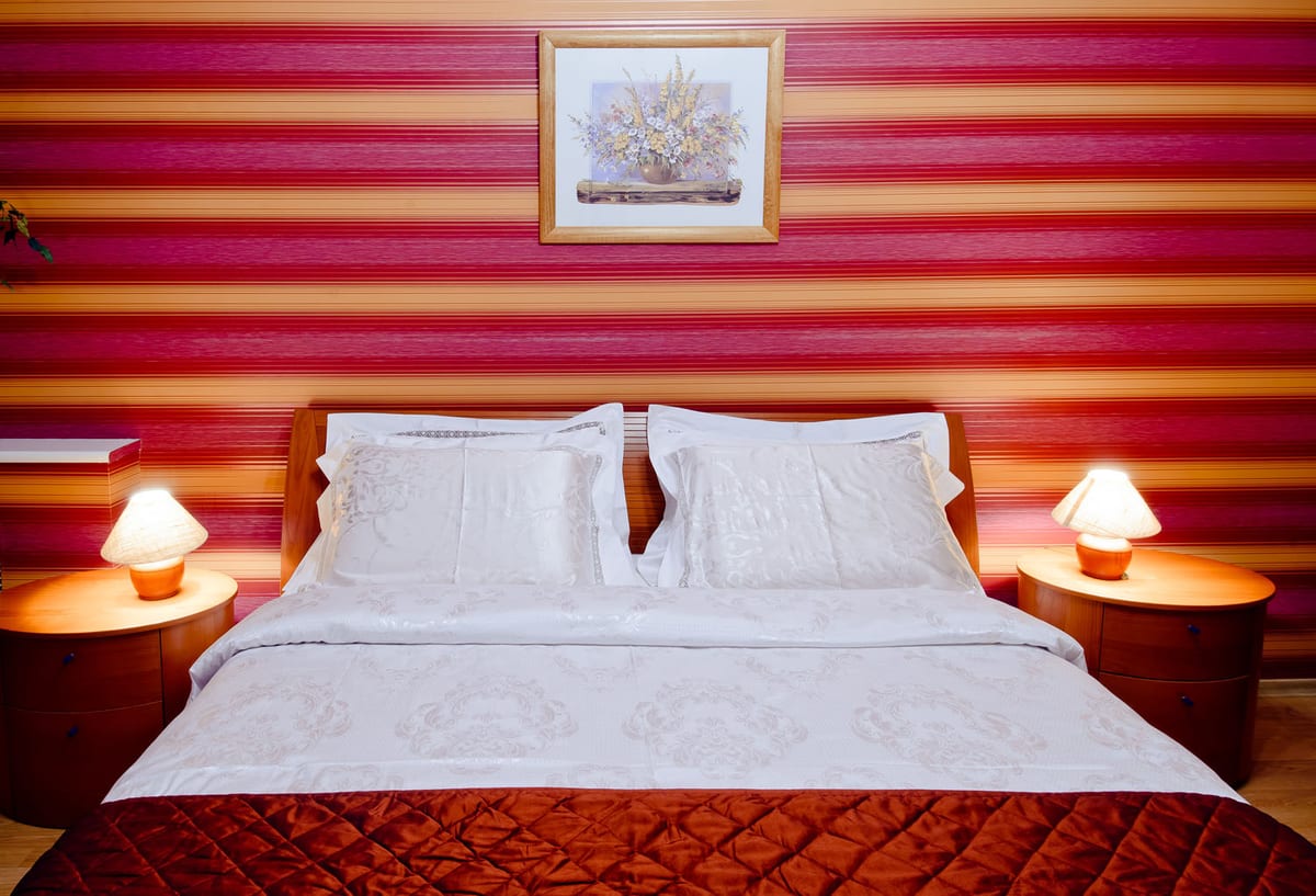Double bed against a raspberry-striped wall between two round bedside lamps