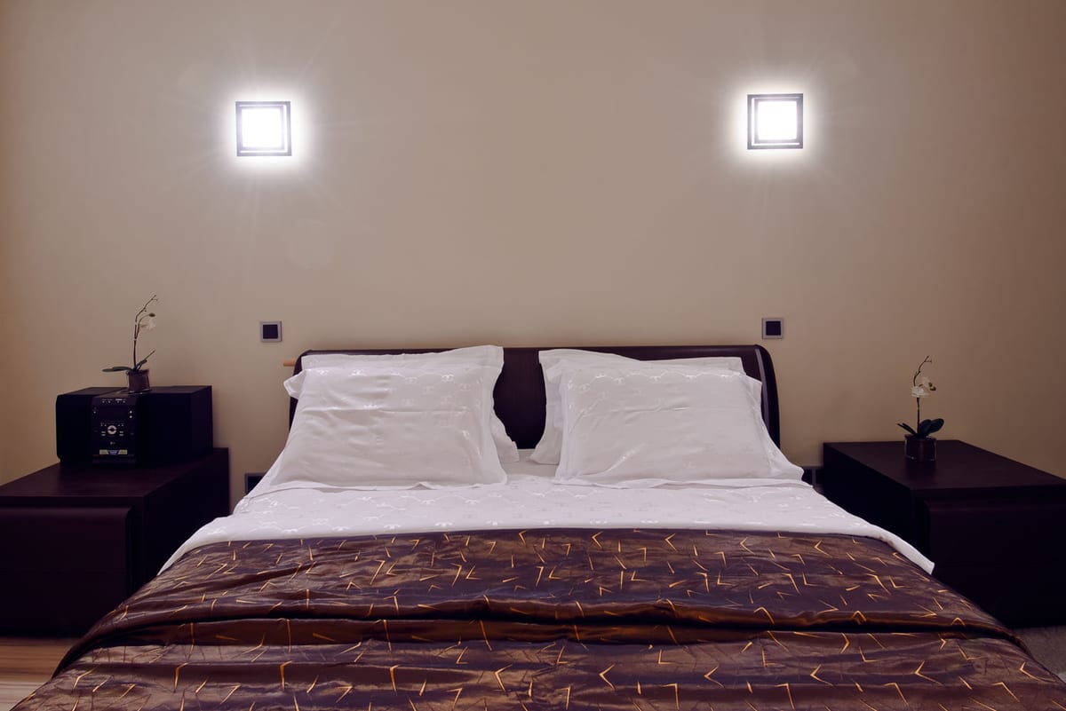Bedroom with a dark headboard, twin bedside cabinets and orchids under square wall lights