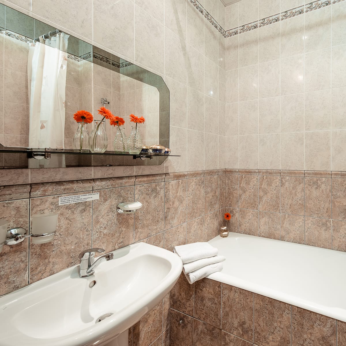 Tiled bathroom with a bath, a basin and orange gerberas on the shelf