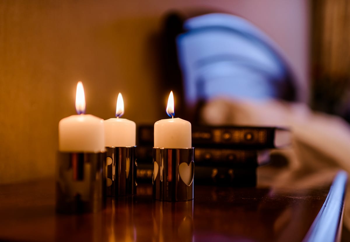 Three lit candles on a bedside table, the bed soft-focus behind