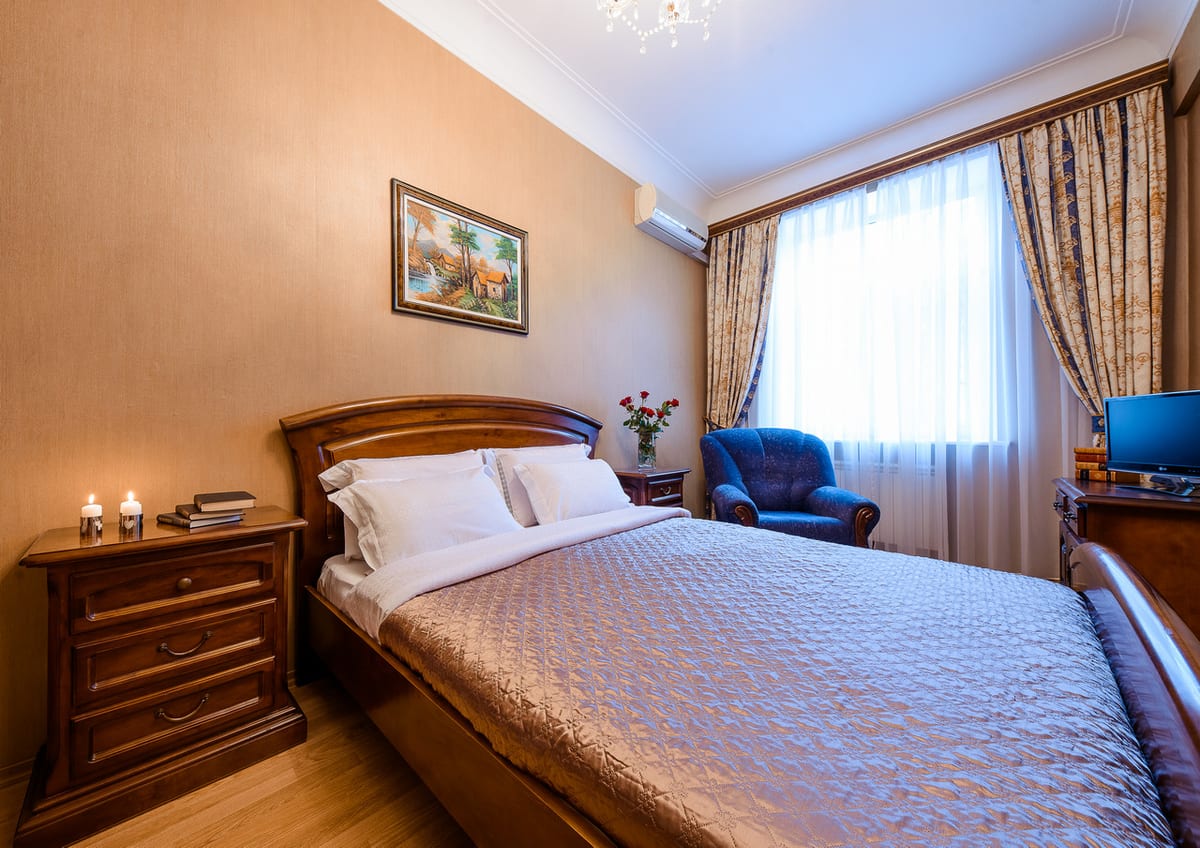Bedroom with a blue armchair by the window, a patterned bedspread and bedside candles