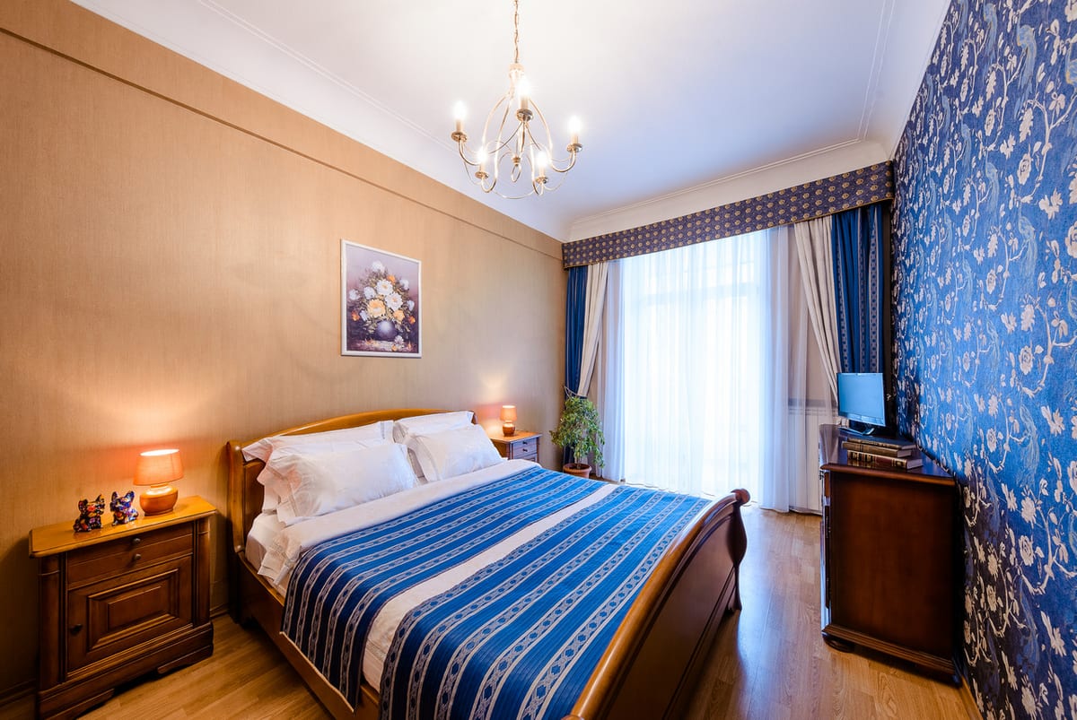 Bedroom with a cobalt damask wall, a chandelier and a blue-and-cream bed runner
