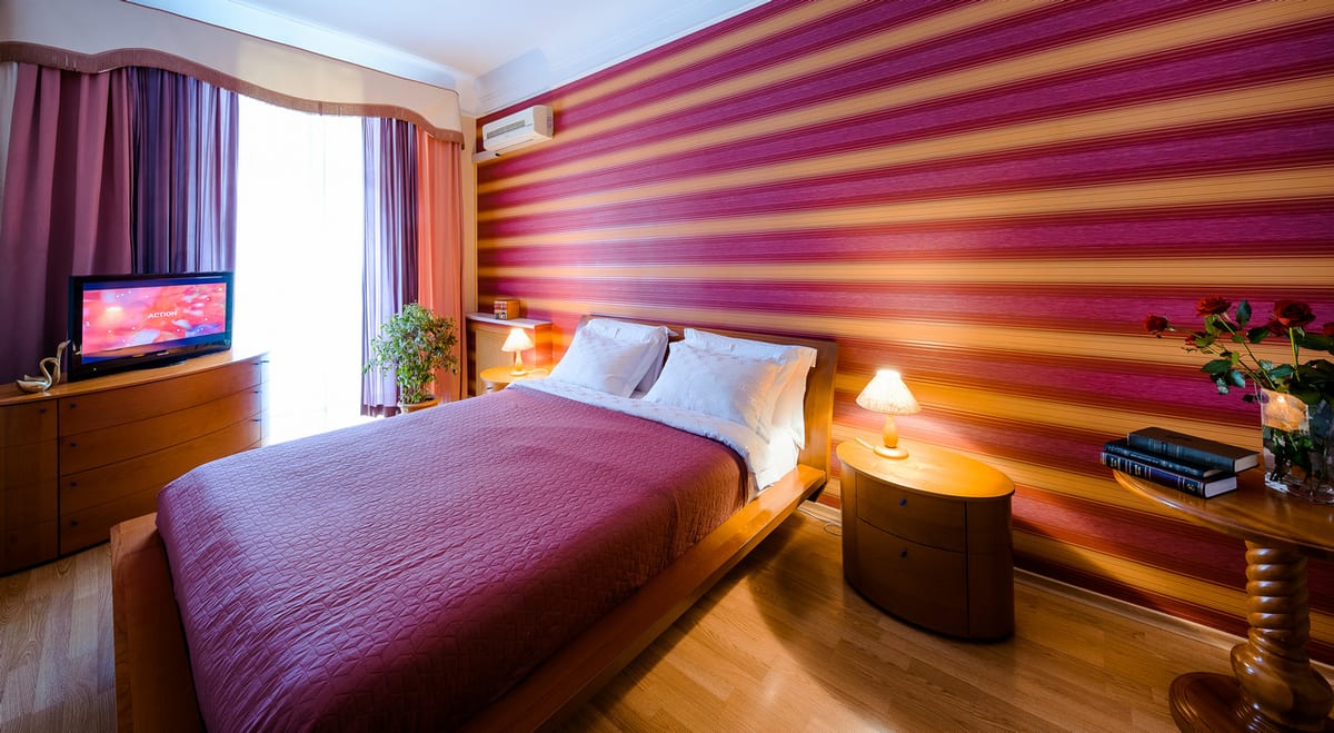 Bed with a plum cover against a purple-and-gold striped wall, television opposite