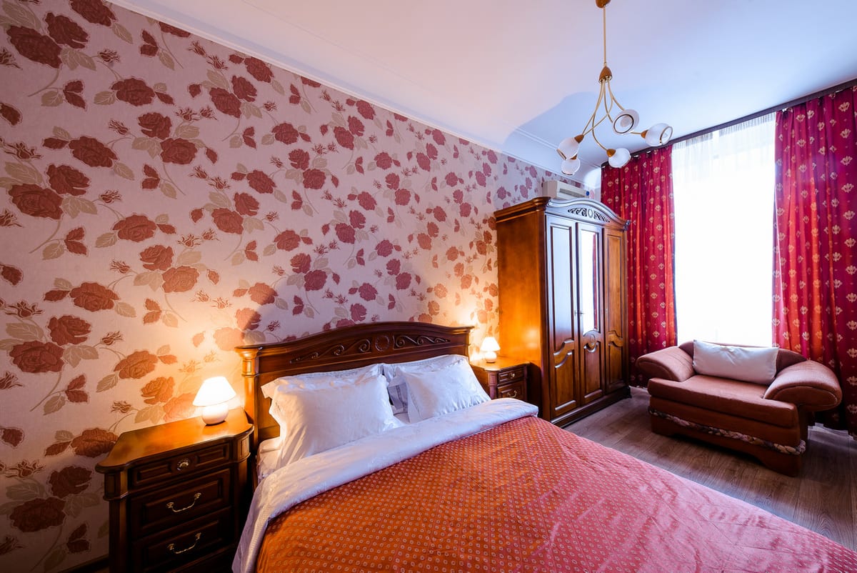 Bedroom with rose-patterned wallpaper, a carved bed, a wardrobe and a chaise longue