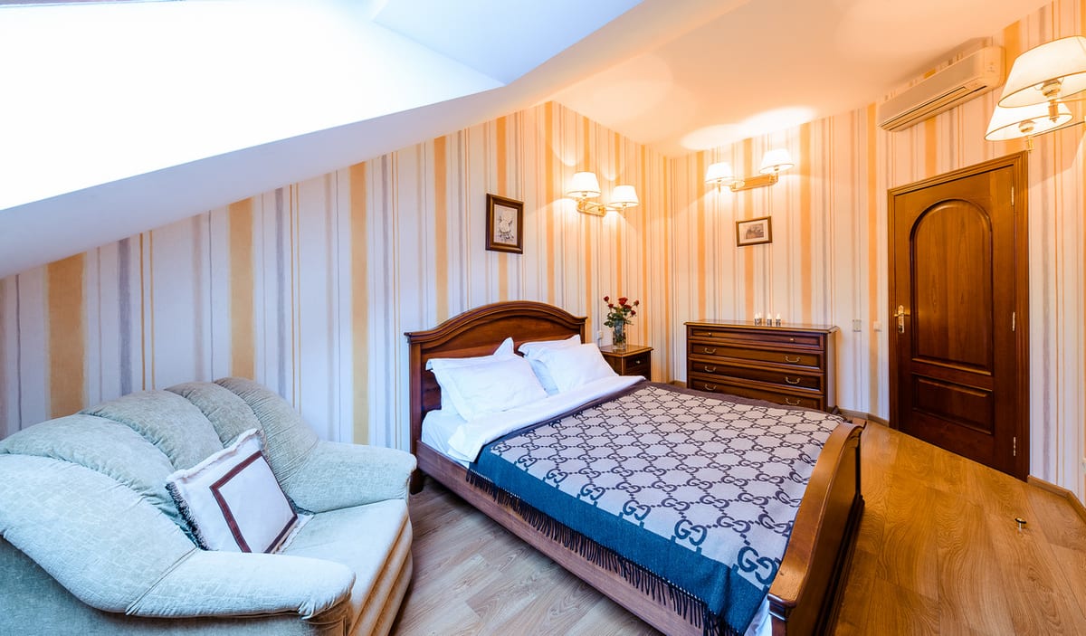 Mansard bedroom in striped wallpaper with a pale sofa alongside the bed