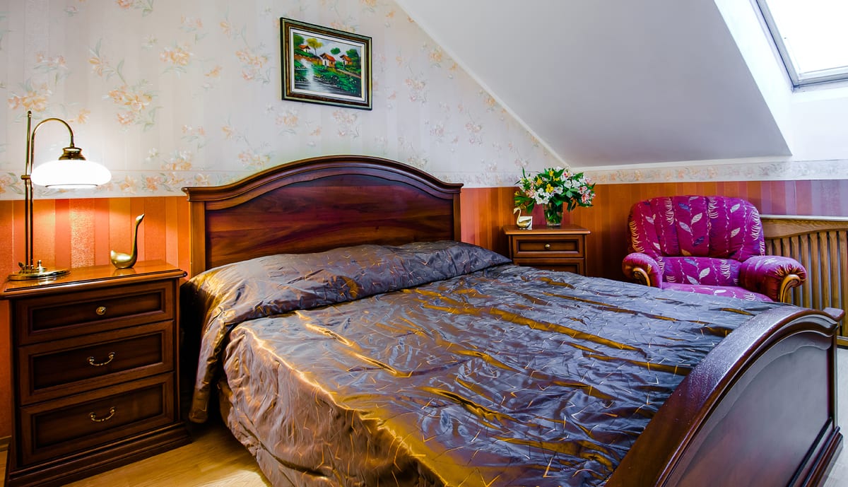 Mansard bedroom with a gold bedspread, a magenta armchair and a skylight overhead