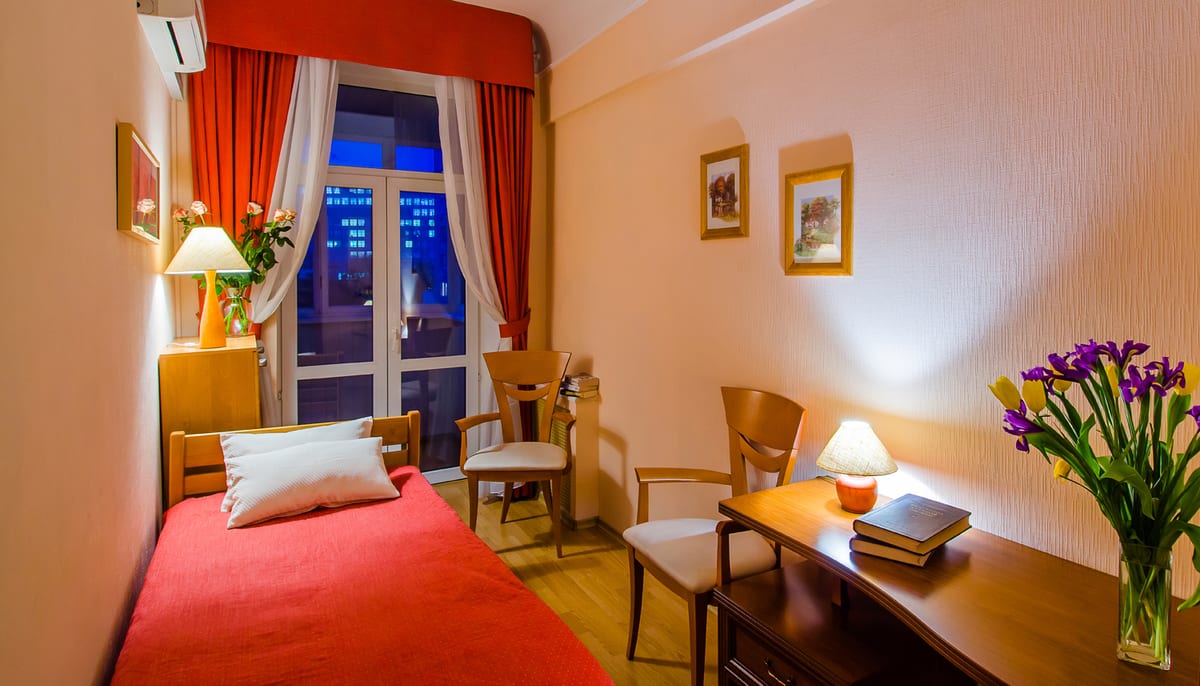 Bedroom at night with red curtains, a writing desk and tulips on the table
