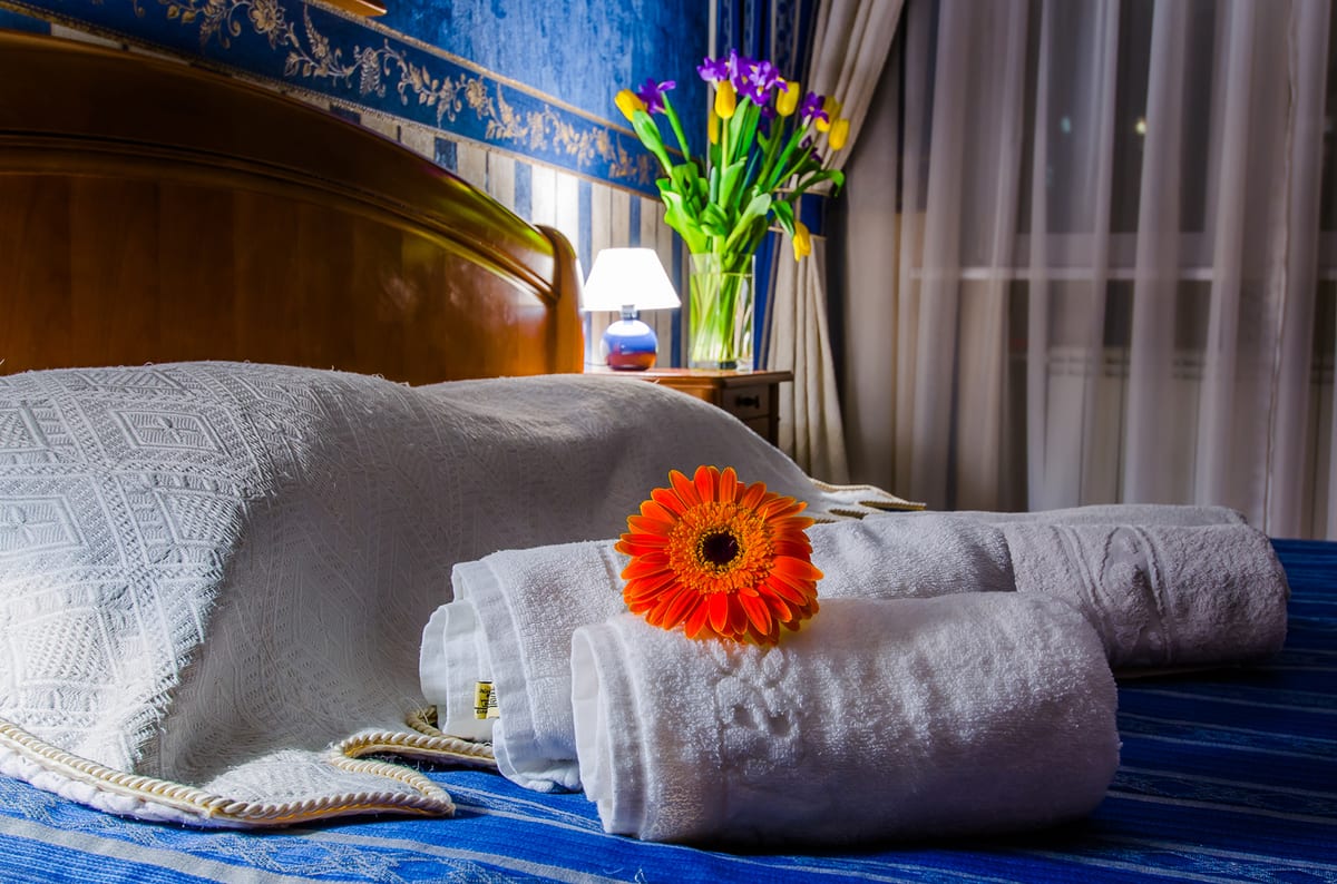 Folded towels and an orange gerbera on a blue bed, tulips behind