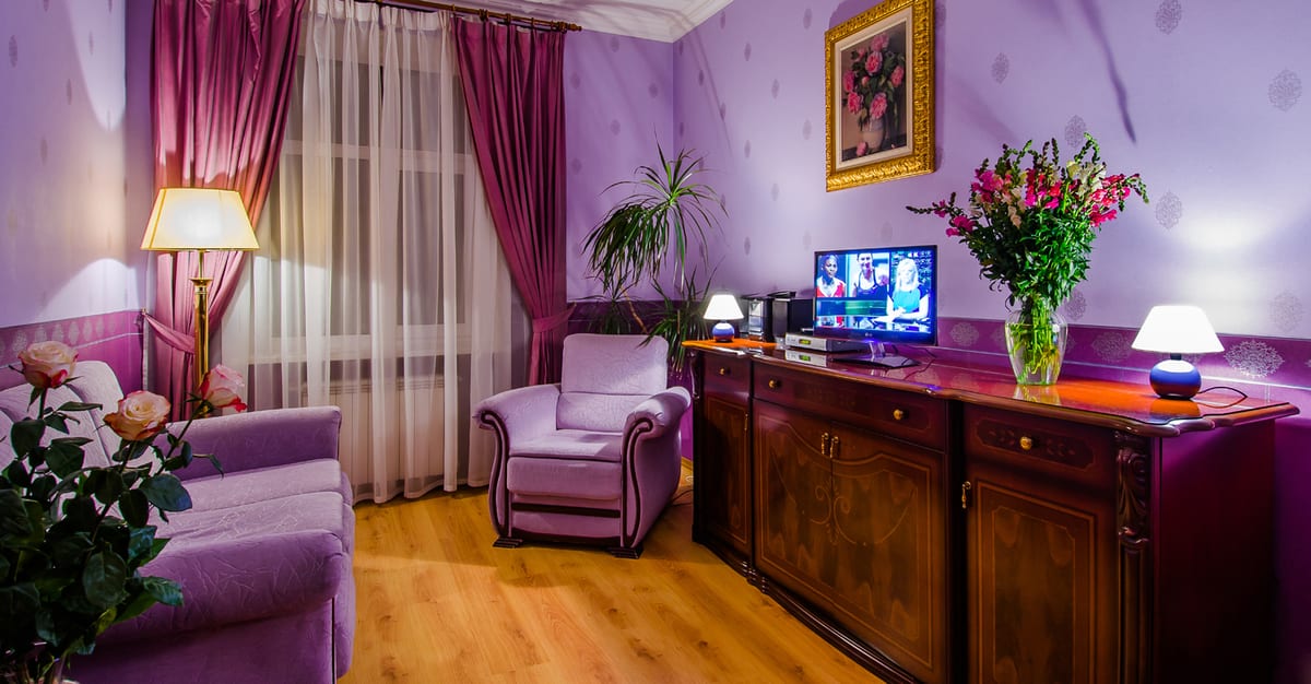 Lilac sitting room with an armchair, a sideboard, a television and cut flowers