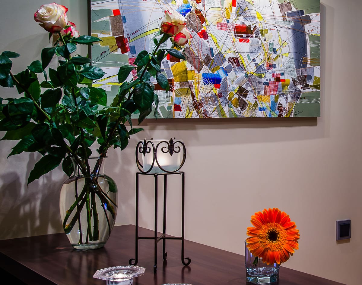 Roses in a glass vase on a wrought-iron stand beneath an abstract canvas