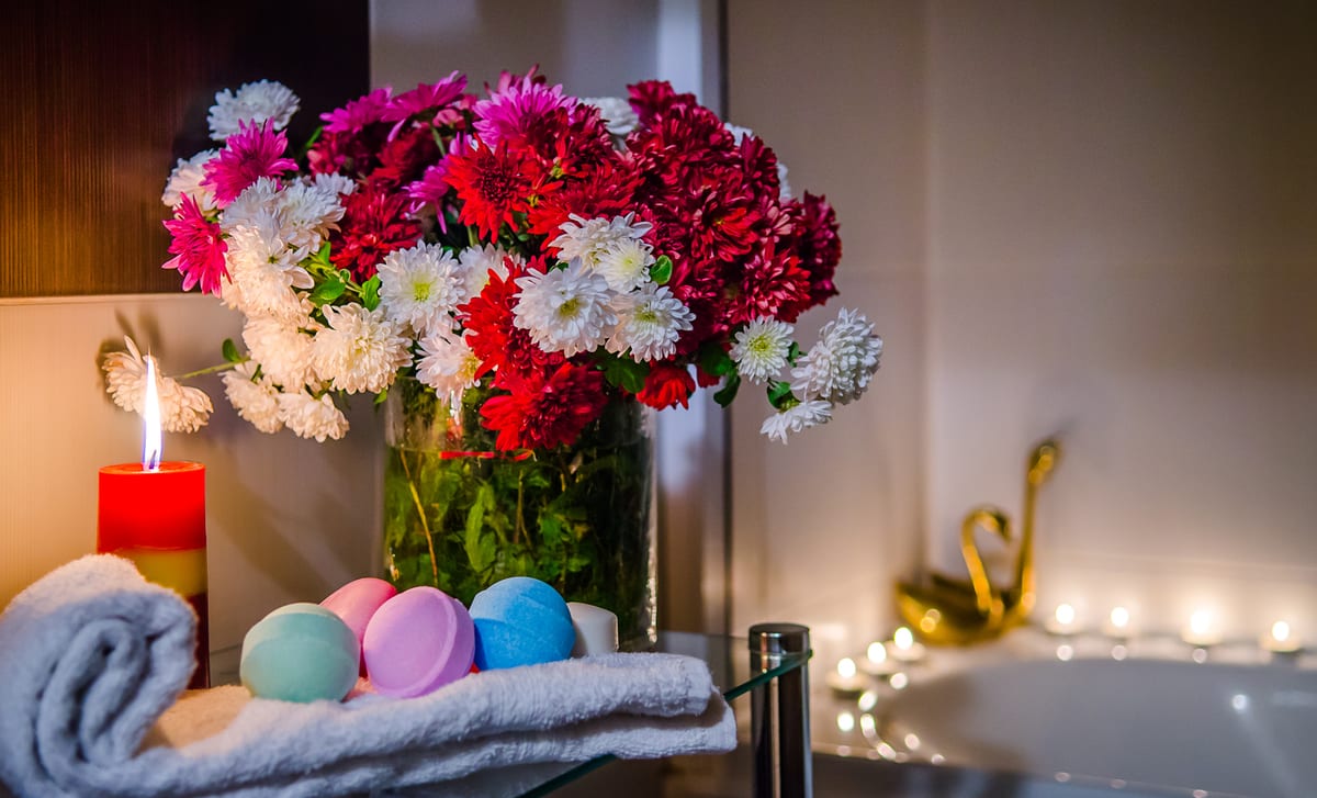 Bath edge set with a candle, bath bombs, folded towels and a bouquet