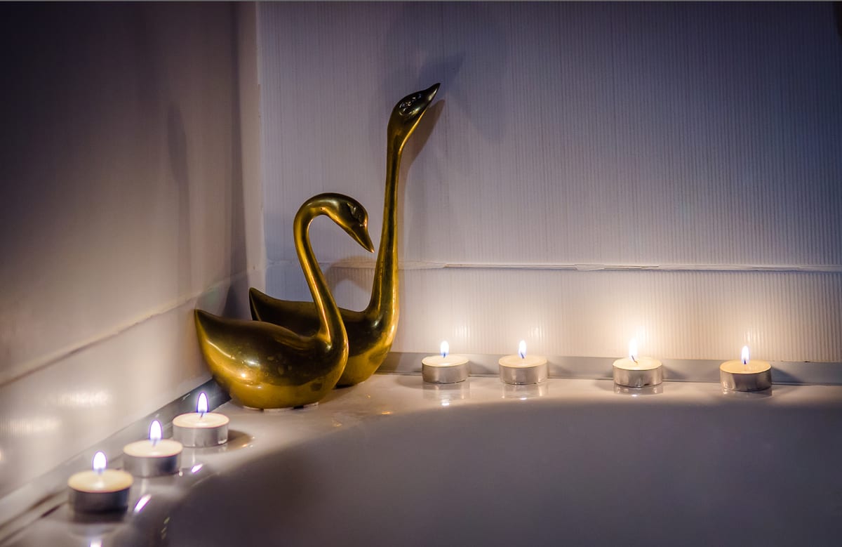 A brass swan and a row of tealights along the edge of a bath