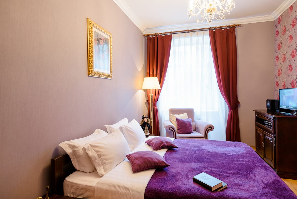 Bedroom with a purple throw, a pink floral wall, an armchair and a television