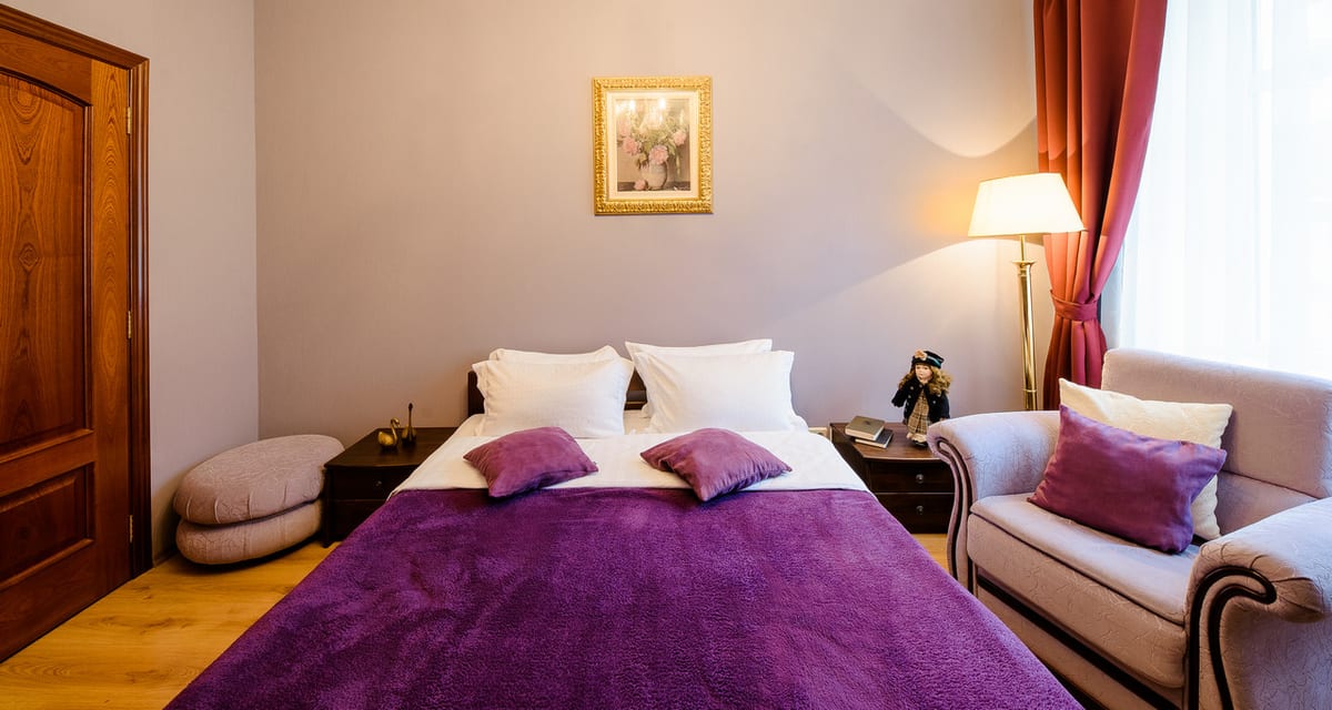 Bedroom with a purple throw across a white bed, a sofa and a footstool