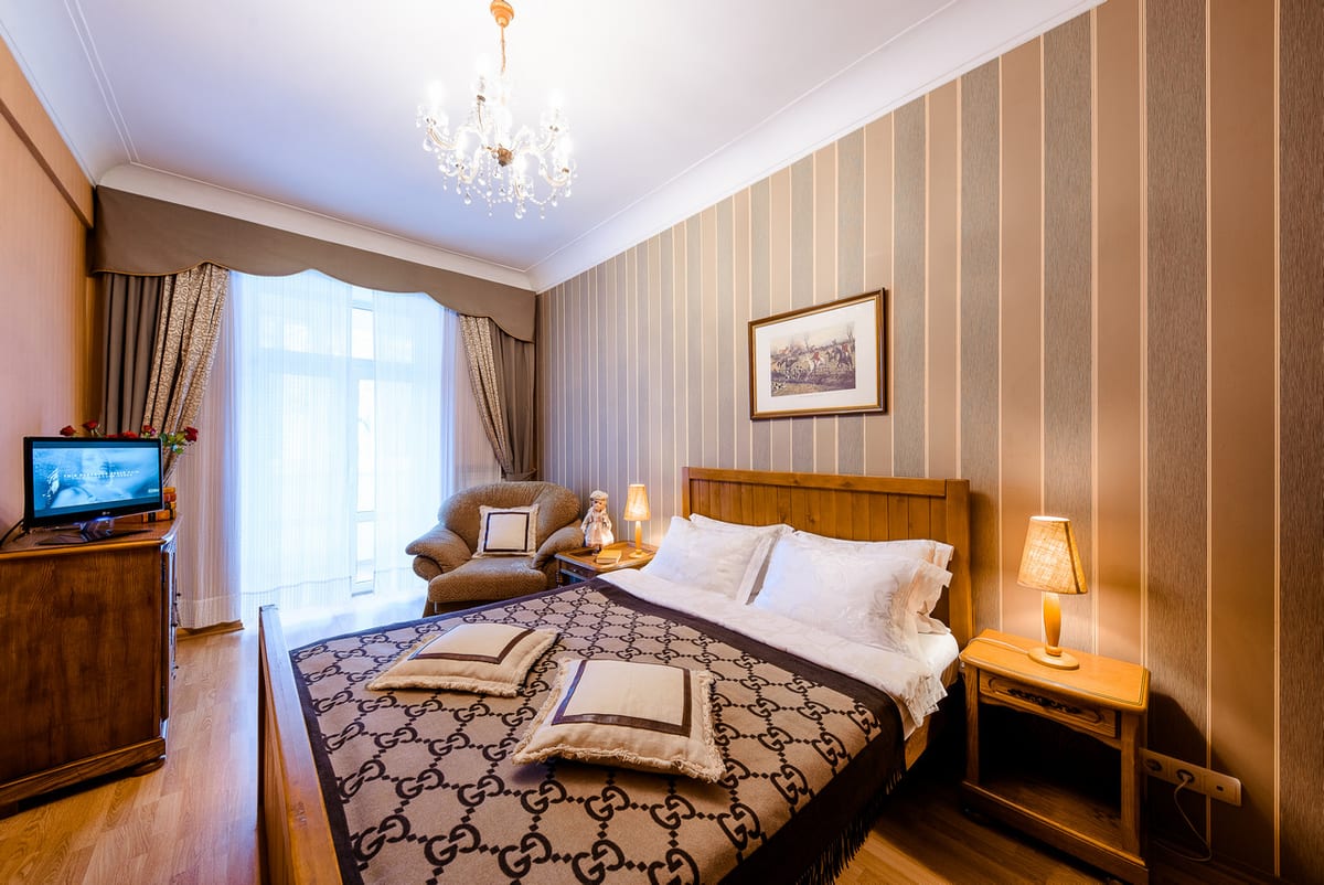 Bedroom with striped wallpaper, a monogrammed bedspread and a television