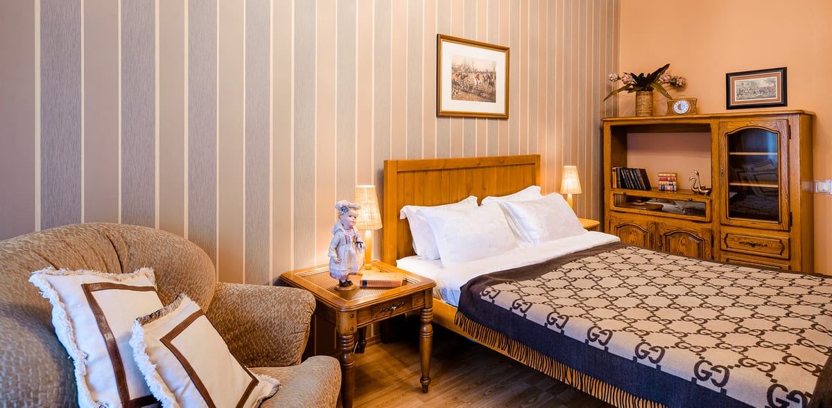 Bedroom with striped wallpaper, an armchair, a bookcase and a monogrammed bed