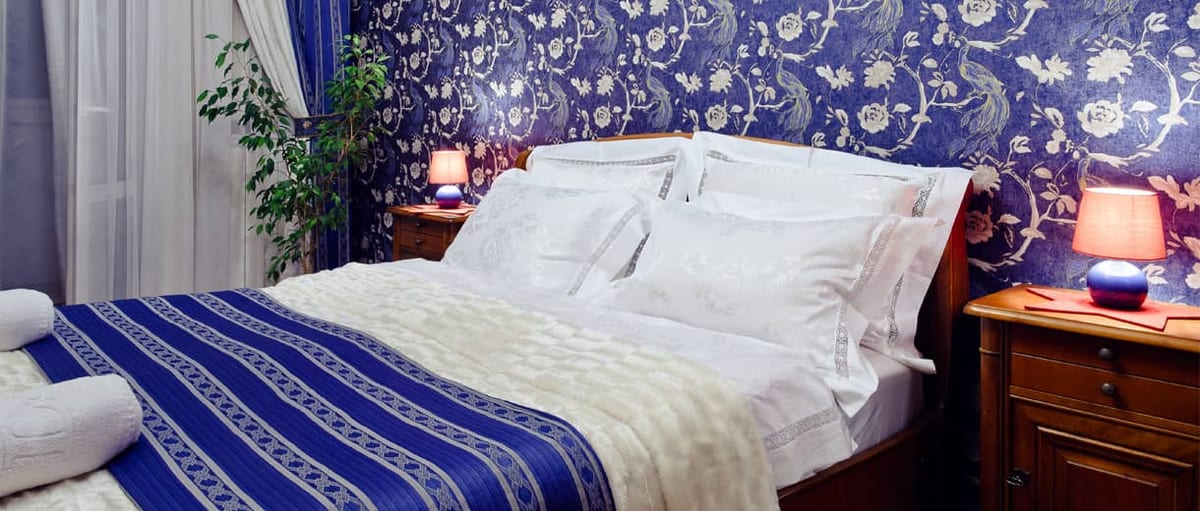 Bed dressed in white with a blue and gold runner against cobalt damask wallpaper