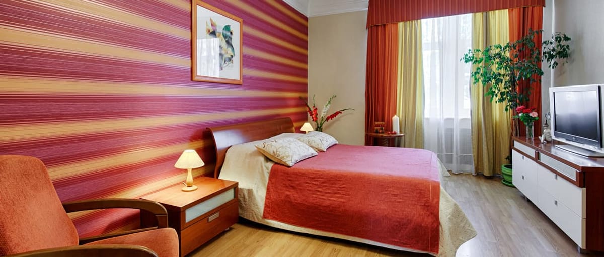 Raspberry-striped bedroom with an orange armchair beside the bed
