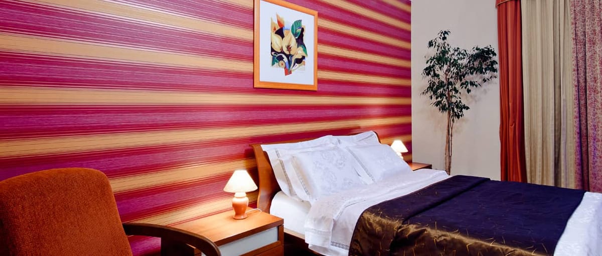 Raspberry-striped bedroom with an orange armchair and a framed print above the bed