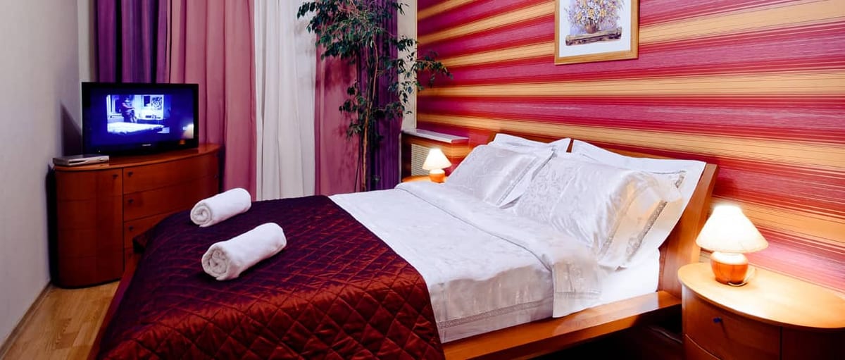 Raspberry-striped bedroom with rolled white towels laid across a claret bedspread