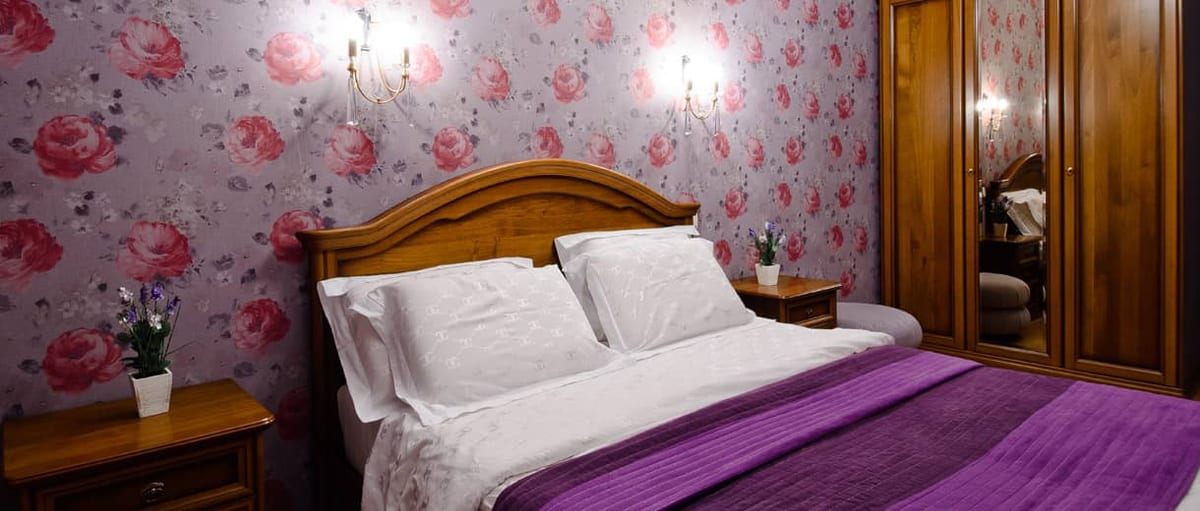 Bedroom with rose-patterned wallpaper and a purple runner laid across the bed