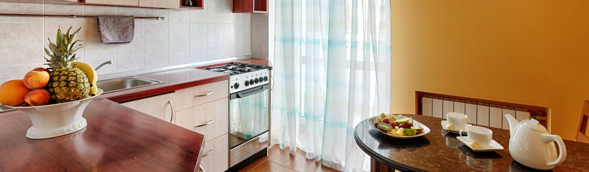 Orange kitchen seen wide, cooker and a table laid with fruit
