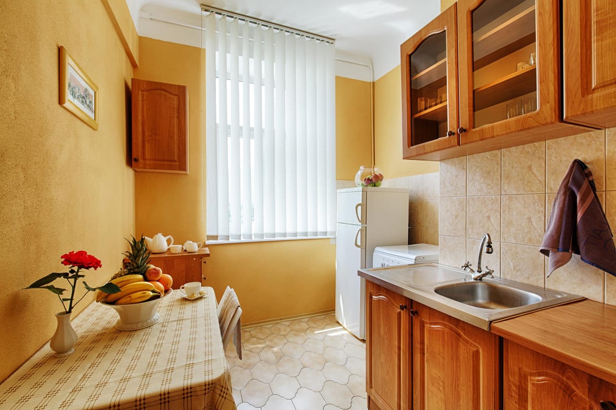 Yellow kitchen with a fridge, a sink and a table of fruit and tea things