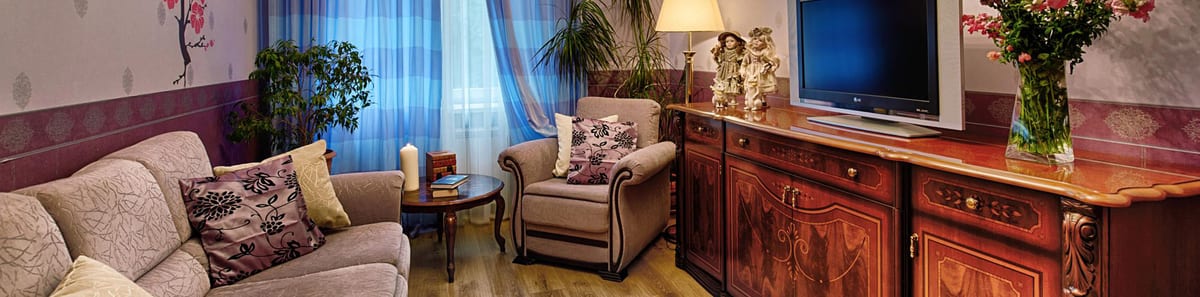 Corner sofa under blue check curtains, a carved sideboard alongside