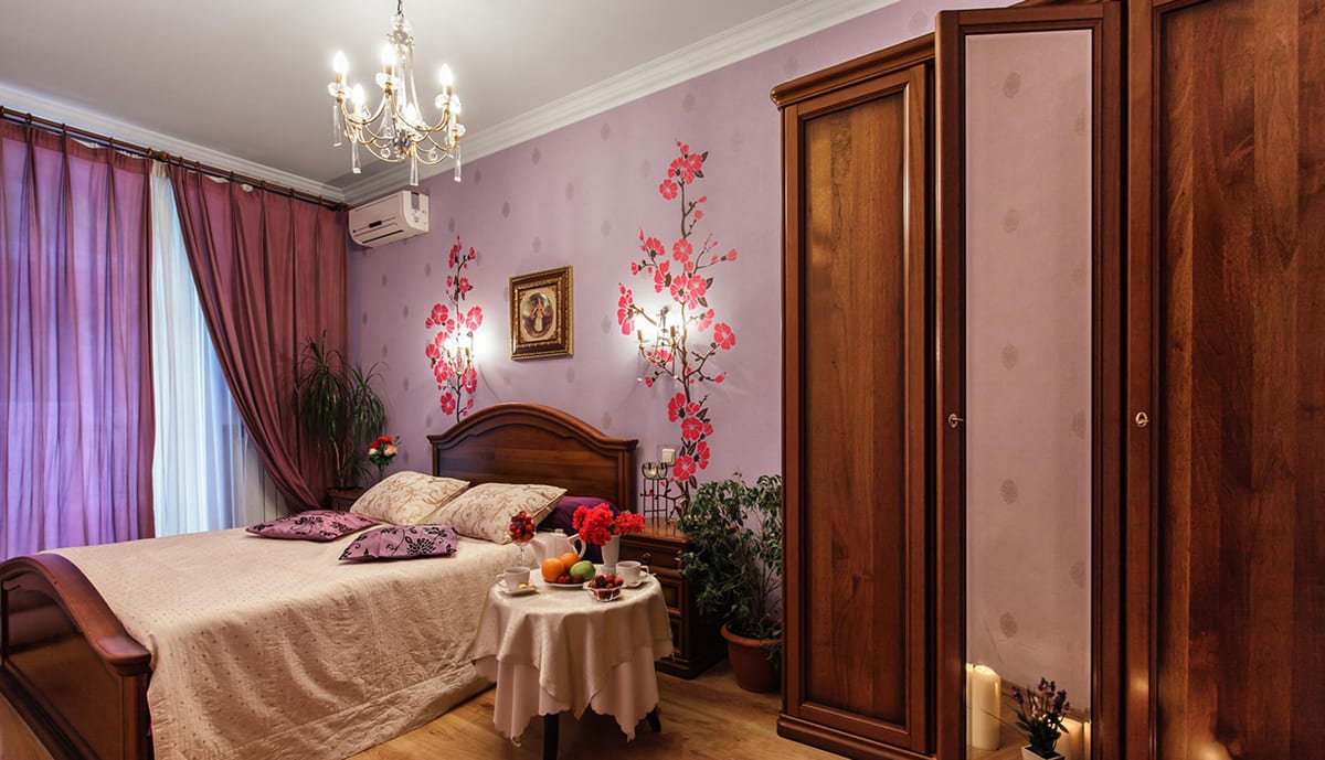 Cherry-blossom wallpaper above a made-up bed, chandelier overhead
