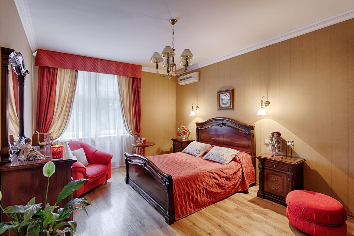 Bedroom with ochre walls, a red bedspread, a red sofa and a carved sleigh bed