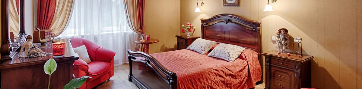 Ochre bedroom seen wide, red bedspread and a red sofa at the foot of the bed