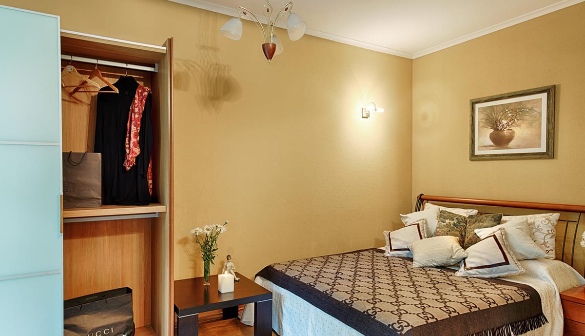 Ochre bedroom with an open wardrobe and a monogrammed throw across the bed