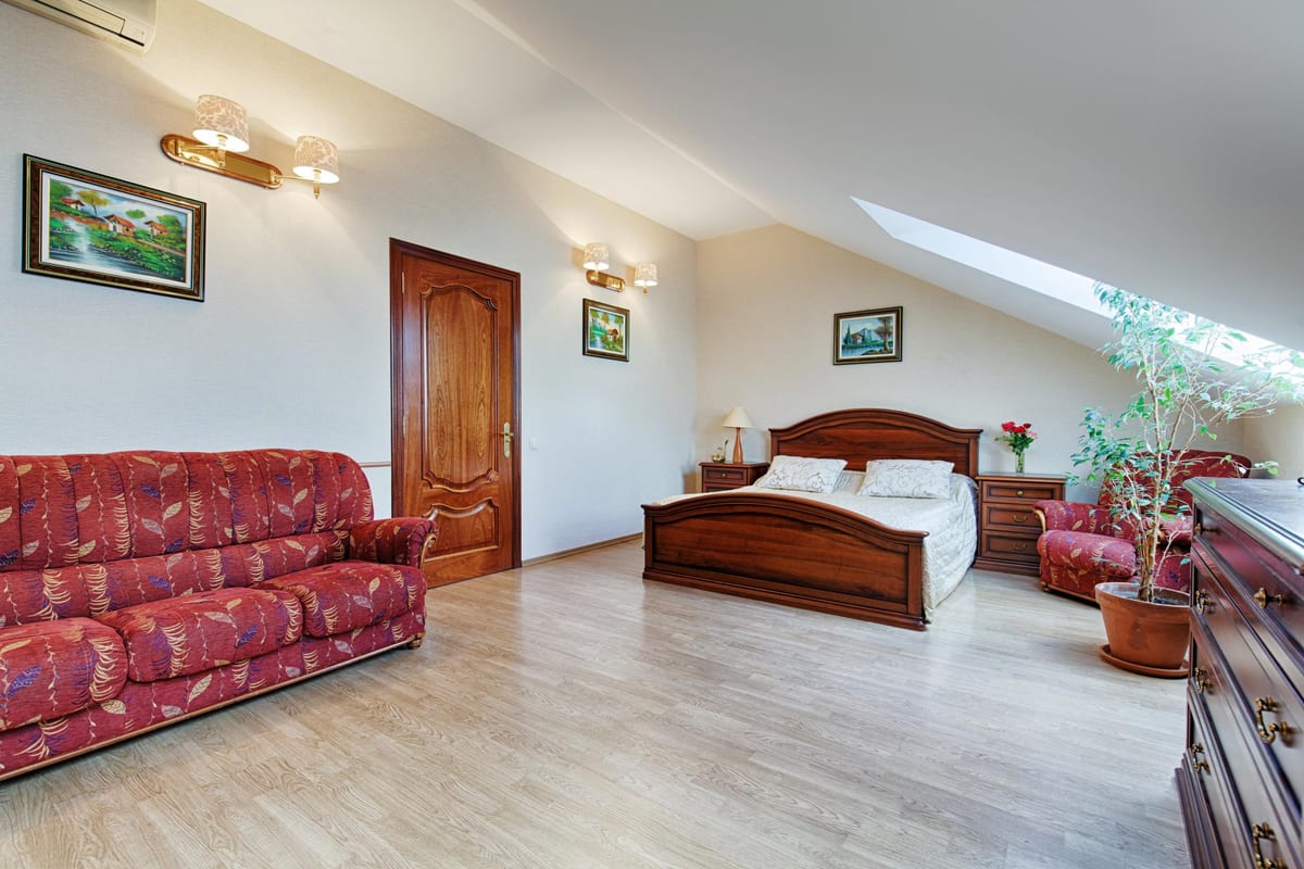 Mansard room with a red patterned sofa, a double bed and a wooden door