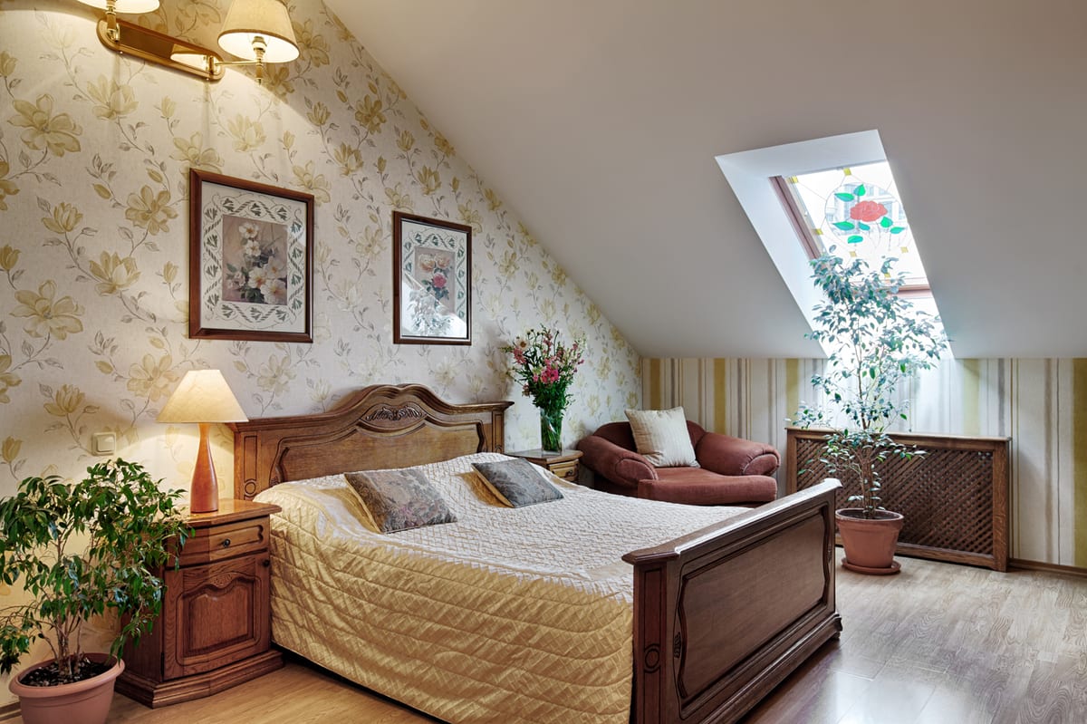 Mansard bedroom with floral wallpaper, a skylight, an armchair and a potted tree