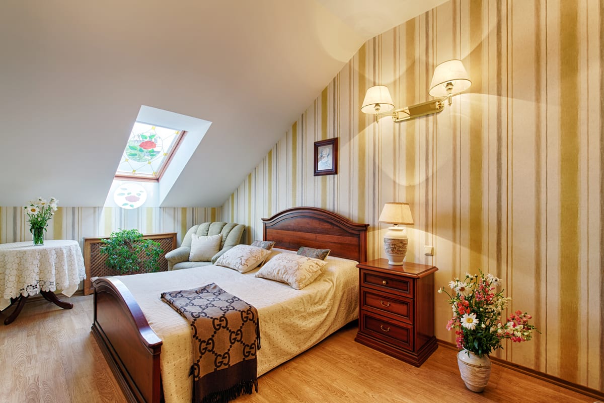 Mansard bedroom in gold stripes, a carved double bed beneath the skylight