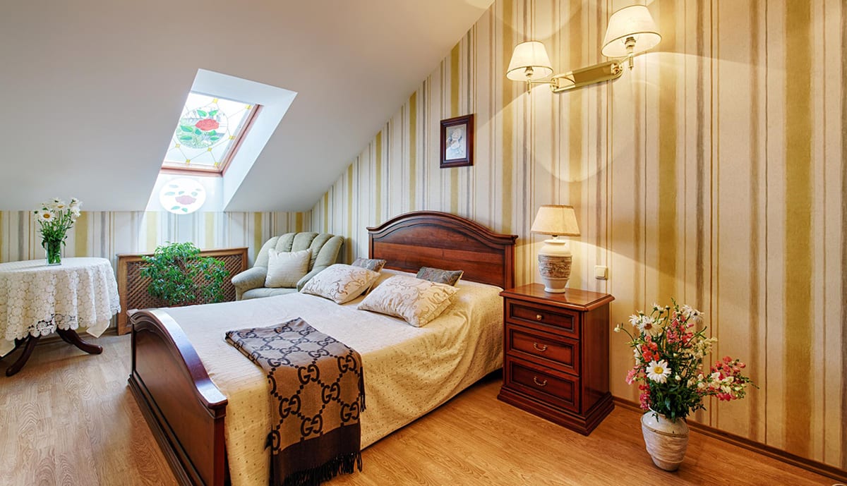 Gold-striped mansard bedroom with a carved double bed under the skylight