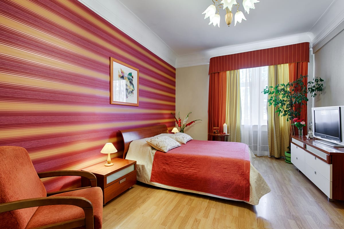 Bedroom with a raspberry-striped wall, an orange armchair and a red bedspread