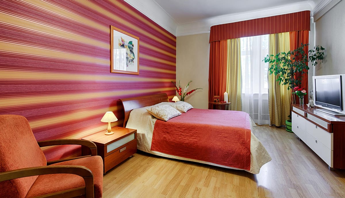 Raspberry-striped bedroom with a red bedspread and an orange armchair