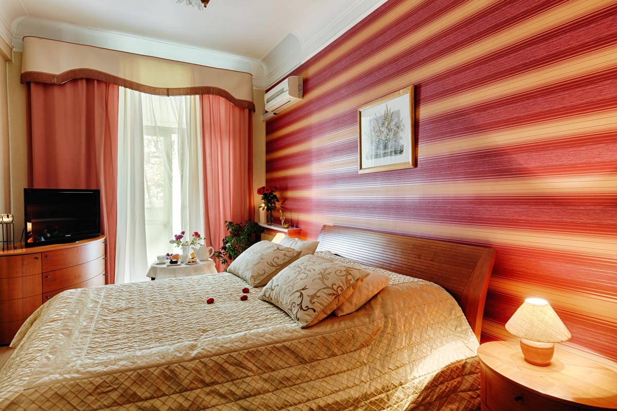 Bedroom with a coral-striped wall, a gold bedspread and a bay window