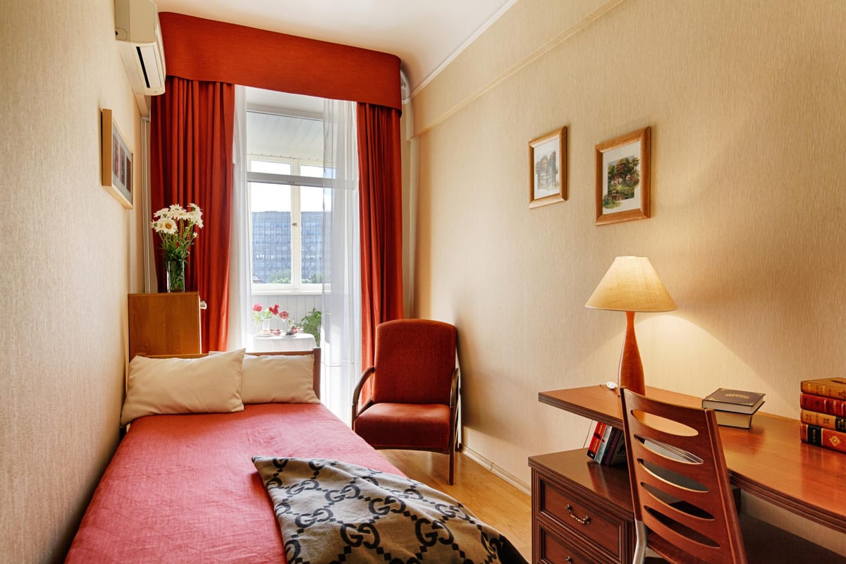 Single room with a coral daybed, a writing desk and books by the window