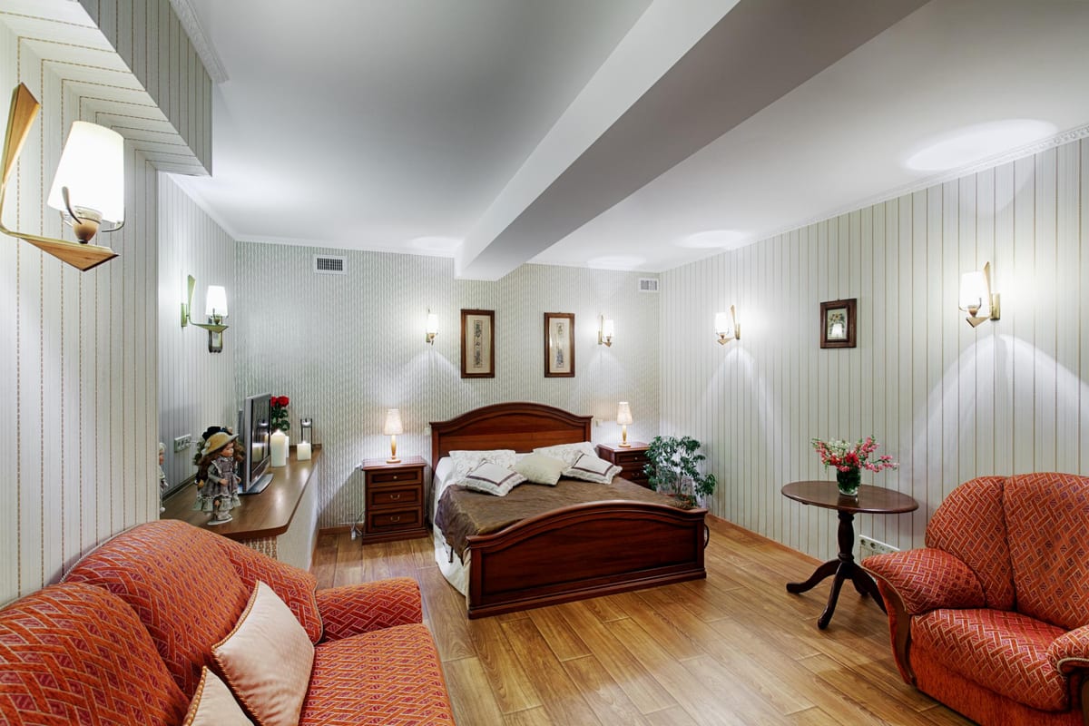 Long room panelled in pale green, a double bed and two coral armchairs