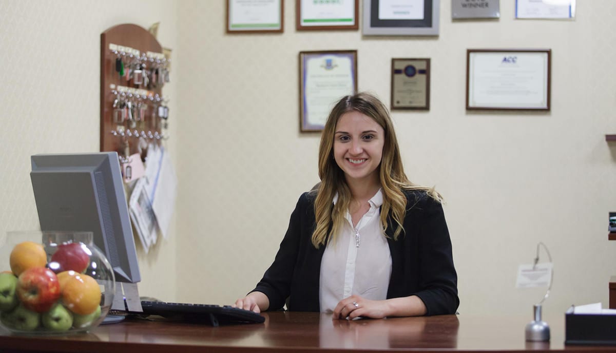 Receptionist at the front desk beneath the key board and framed certificates