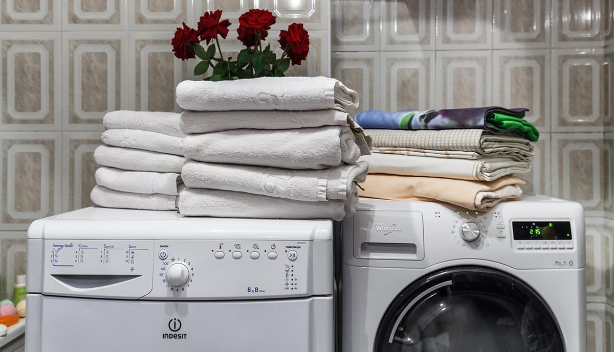 Washing machines with folded towels and linen stacked on top, red roses alongside